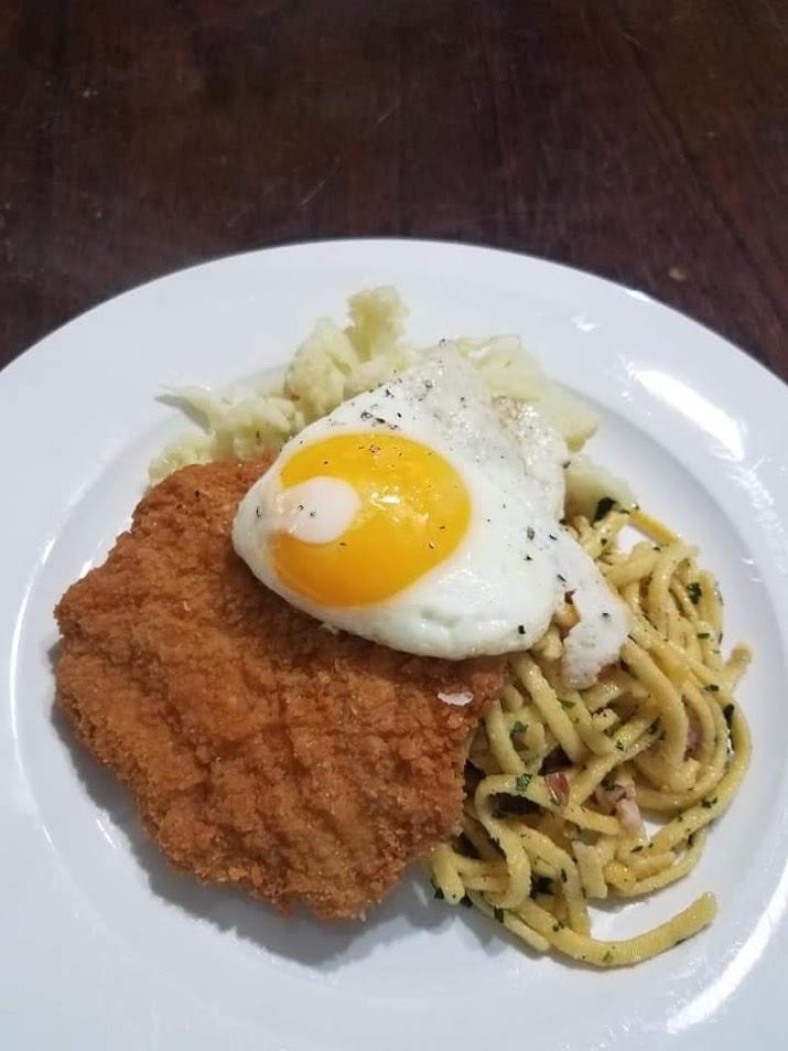 Breaded cutlet with fried egg and pesto pasta