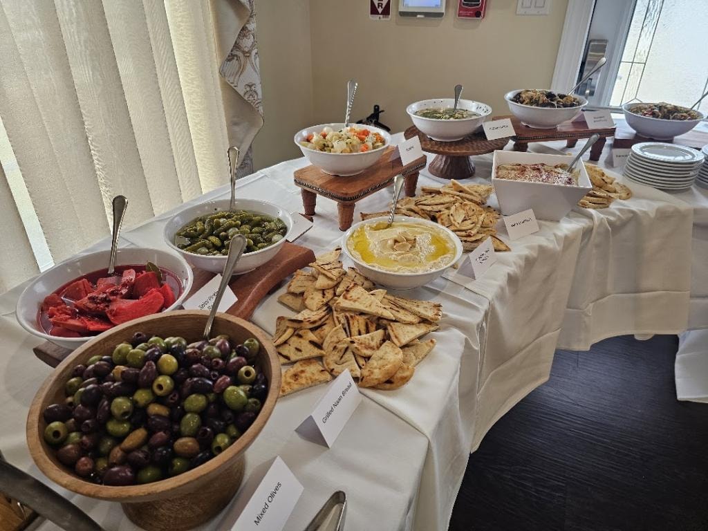 Mediterranean-style catered buffet with salads, dips, olives, and pita bread