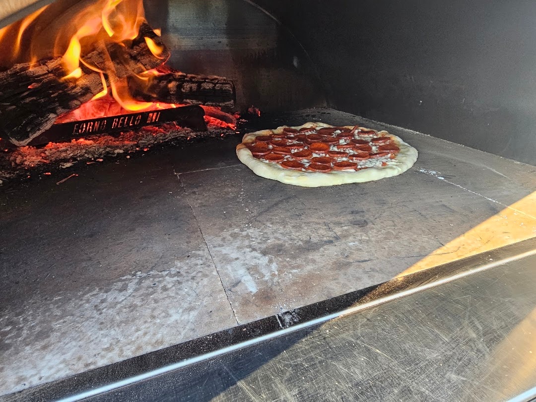 Pepperoni pizza cooking in wood-fired oven